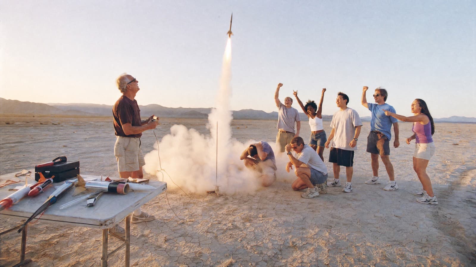 Friends cheering as a model rocket launches off a dry lakebed at golden hour